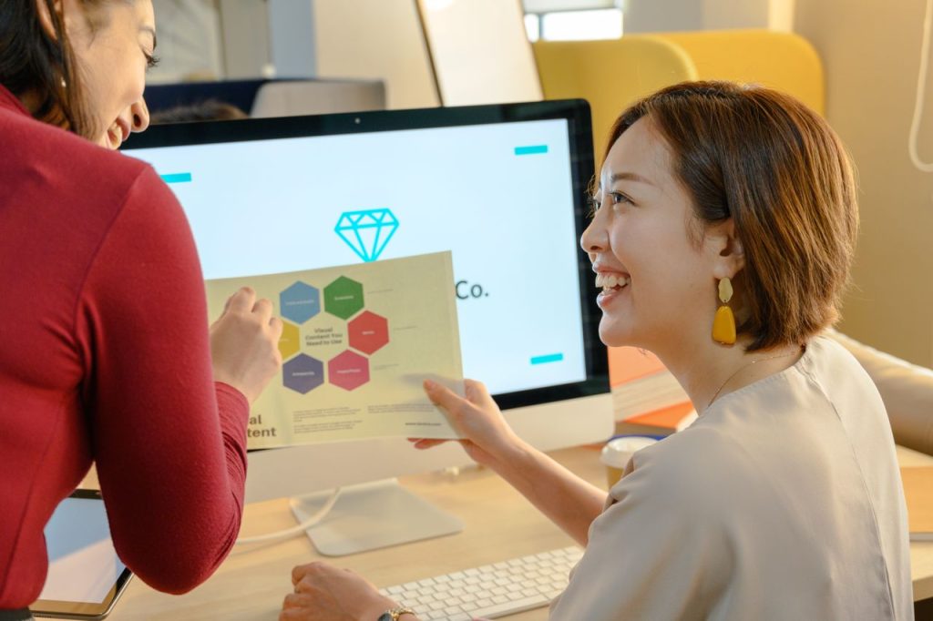 Two women discussing a report on a computer screen, fostering teamwork in a modern office setting.
