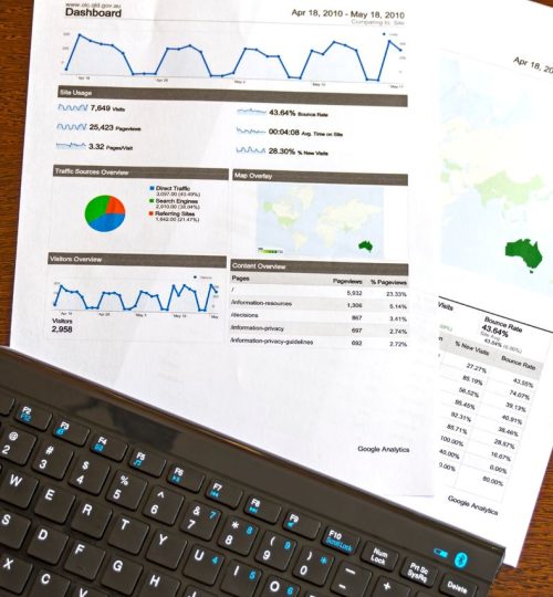 Flatlay of a business analytics report, keyboard, pen, and smartphone on a wooden desk.